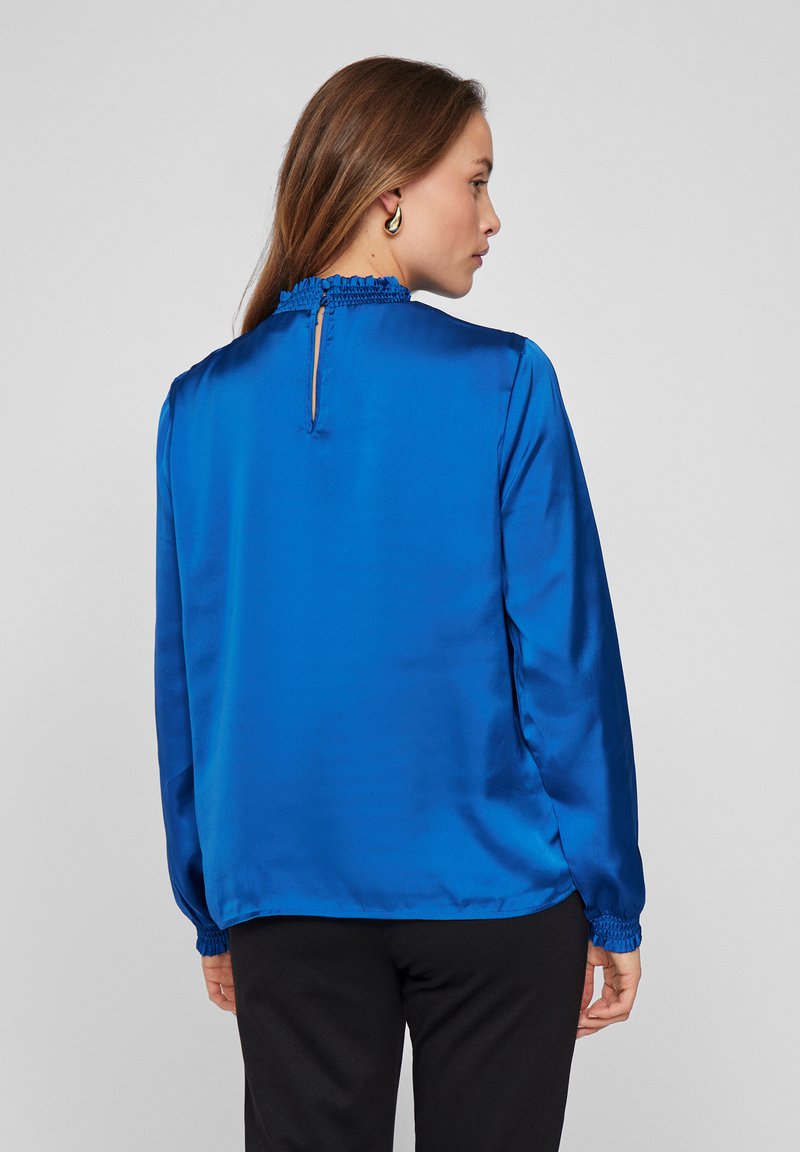 Blauwe satin blouse met een hoge hals en gerimpelde rand, met lange mouwen met elastische boorden en een keyhole detail op de rug.