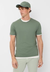 Maglietta verde oliva a maniche corte con dettagli bianchi nel collo e nelle maniche, abbinata a pantaloni verde chiaro. Design semplice e aderente.