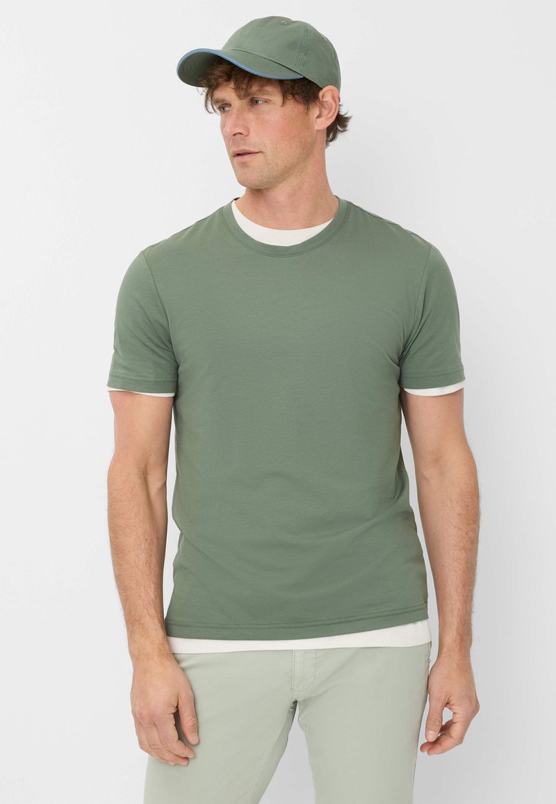 Maglietta verde oliva a maniche corte con dettagli bianchi nel collo e nelle maniche, abbinata a pantaloni verde chiaro. Design semplice e aderente.