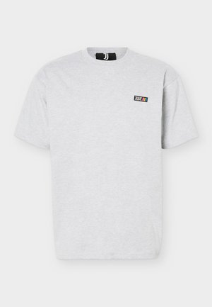 Ανοιχτό γκρι μπλουζάκι με κοντά μανίκια και στρογγυλή λαιμόκοψη, με μικρό ορθογώνιο λογότυπο "JUVE" και τρεις κάθετες έγχρωμες ρίγες στο αριστερό στήθος.