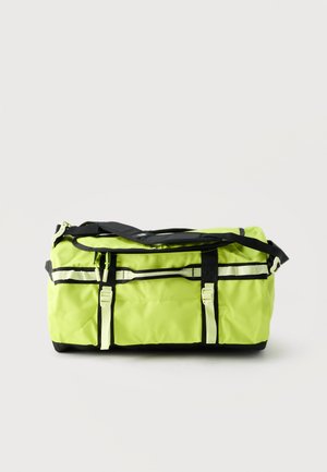 Bolsa deportiva de lona de color amarillo brillante con correas negras, dos hebillas frontales, bolsillos con cremallera y correa ajustable para el hombro sobre un fondo liso.