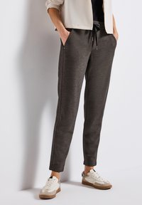 Joggers gris, fuselés avec une taille élastique à cordon, poches latérales, et tissu texturé ; portés avec des sneakers blancs et beiges.