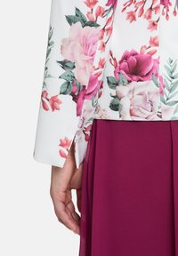 Kurtka w kwiatowy wzór w białym kolorze z różowymi i zielonymi kwiatami, w połączeniu z ciemnoczerwoną spódnicą. Posiada dopasowany krój i gładką teksturę.