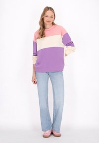 Felpa a blocchi di colore nei toni di rosa, crema e viola; tessuto morbido con un fit rilassato. Abbinata a jeans svasati di un blu chiaro e scarpe rosa.