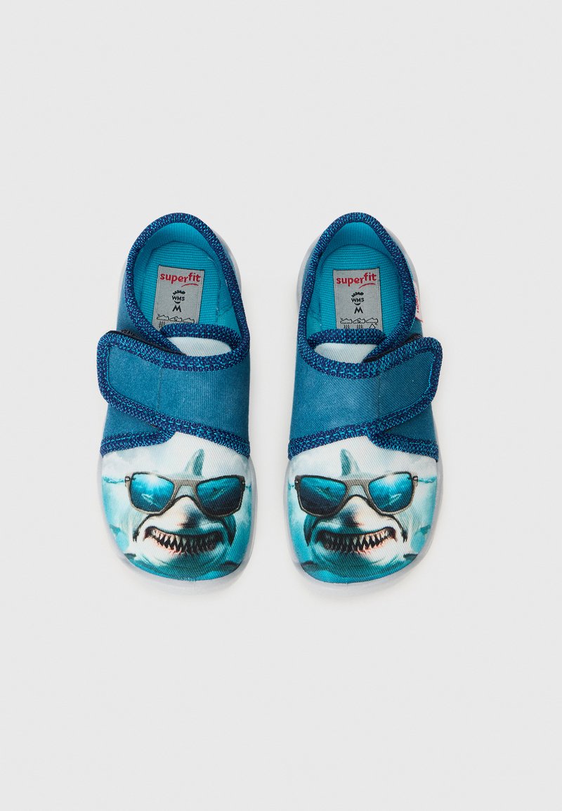 Kinderschuhe mit einem Obermaterial aus blauer Stoff, das im Zehenbereich eine Haifigur mit Sonnenbrille zeigt, sowie einem Klettverschlussriemen.