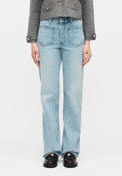 Άτομο που φοράει ανοιχτό γαλάζιο τζιν ψηλόμεσο με ίσιες ποδιές, σκούρα δερμάτινα μοκασίνια με μεταλλική λεπτομέρεια και γκρι σακάκι με κουμπιά, εμφανιζόμενο από μπροστά.