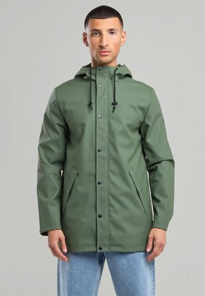 Veste imperméable vert olive avec fermeture à boutons-pression à l'avant, capuche ajustable et poches latérales, présentant une texture lisse et élégante.