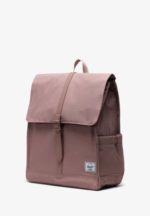 Pale pink backpack made of durable fabric. Features a flap with a buckle closure, side pocket, and a brand label on the front.