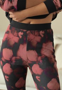 High-waisted leggings in a textured fabric featuring a black base with large pink and red floral patterns, accented by black waistband.