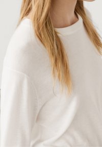 Maglione bianco a maniche lunghe in maglia con collo rotondo, caratterizzato da una texture morbida e liscia e da una vestibilità comoda, mostrato parzialmente su un modello.
