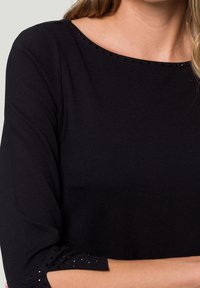 Blouse noire en tricot avec des manches trois-quarts, ornée de perles décoratives le long de l'encolure et des bords des manches. Texture lisse, coupe classique.