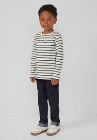 Gestreepte lange mouwen shirt in wit en donkergrijs, gecombineerd met donkerblauwe jeans en witte sneakers met bruine zolen.