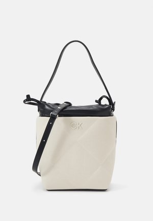Bolso beige y negro con correa negra ajustable para el hombro y logo "CK" en relieve en la parte frontal de tela beige.