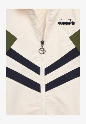 Giacca bianca con strisce a chevron nere, dettagli verdi sulle spalle, una cerniera con tiretto circolare argentato e il logo "diadora" nero sul petto.