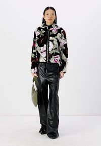 Faux fur jacket with floral pattern in black, white, pink, and green, paired with black leather pants and a green handbag.