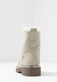 Botín de ante beige hasta el tobillo con un collar blanco peludo, tacón texturizado marrón y un sutil detalle de costura en la parte trasera. Diseño de puntera redonda.