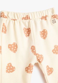 Leggings de crema clara con una textura suave, que presentan un estampado de corazones en todo el tejido en óxido y lunares blancos. Cintura elástica con una etiqueta.