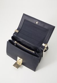 Marineblaues strukturiertes Lederhandtasche mit einem goldenen Metallverschluss und Reißverschluss. Geräumiges Innere mit einem dunklen Stofffutter und mehreren Fächern.