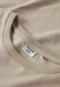 Collo del maglione a girocollo beige a coste con etichetta del marchio visibile che riporta "Two Spoon, 11-12Y, 146-152".