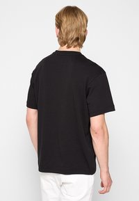 T-shirt en coton noir avec manches courtes et col rond. Texture lisse, coupe décontractée, sans motifs ni graphismes visibles.
