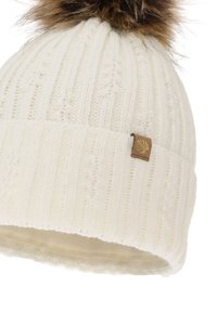 Berretto in maglia bianco con un motivo a coste, caratterizzato da una grande pompon in pelliccia sintetica marrone sulla parte superiore e un piccolo etichetta in tessuto marrone con un logo.