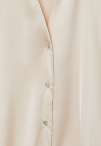 Blush pink blouse featuring a smooth, satin-like texture with a v-neckline, eight clear buttons, and a relaxed fit design.