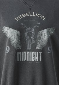 Šedé tričko z uhlíkové barvy má grafiku motocyklu s křídly, ozdobené hroty, a text „REBELLION“ a „MIDNIGHT.“