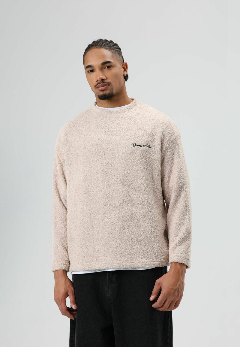 Beige fleece sweater met lange mouwen en een ronde hals; heeft een klein zwart logo op de borst; zachte textuur en een ontspannen pasvorm.