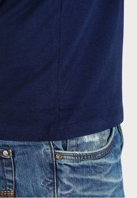 T-shirt in cotone blu navy con maniche corte, dotato di orlo dritto e cuciture laterali, abbinato a jeans in denim blu leggermente usurati.