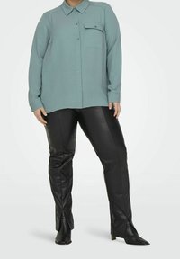 Světle modrá košile s dlouhým rukávem a kapsou na hrudi, spárovaná s černými koženými slim kalhotami s předními rozparky a špičatými černými botami.