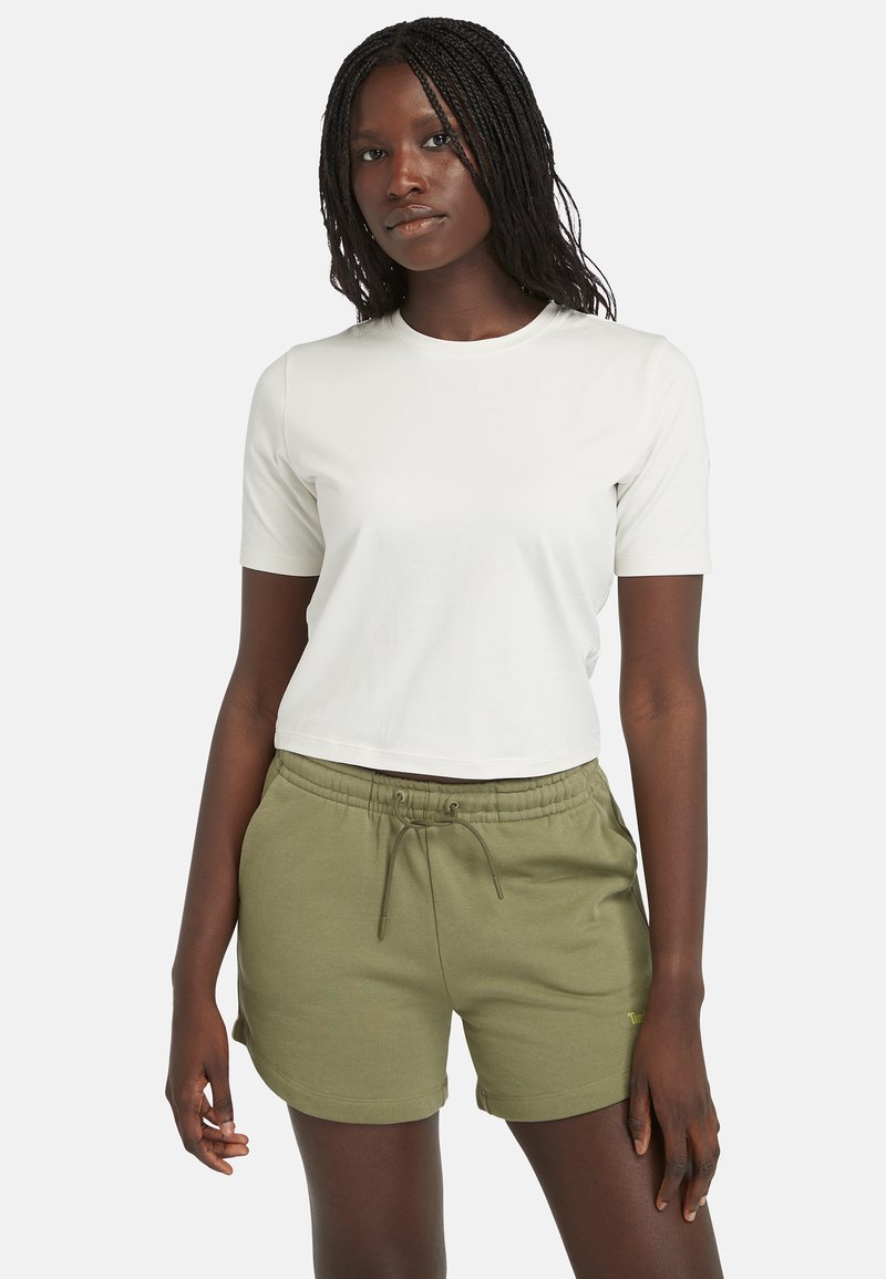 Camiseta blanca corta de manga corta, combinada con pantalones cortos verde oliva con cordón. Tejido suave con un ajuste relajado y bolsillos laterales.