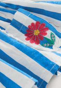 Striped fabric in blue and white, featuring red embroidered flower detail with yellow center and green leaves. Soft, lightweight cotton material.