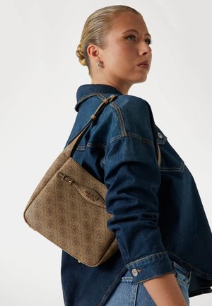 Borsa a tracolla marrone con una trama firmata, dotata di una lunga cintura regolabile e una tasca con zip, indossata su una giacca di jeans.