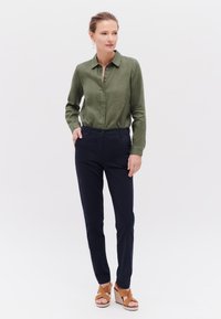 Olivgrön knapp-up skjorta, marinblå slim-fit byxor och tan platta sandaler; mjuk tyg och klassisk krage design.