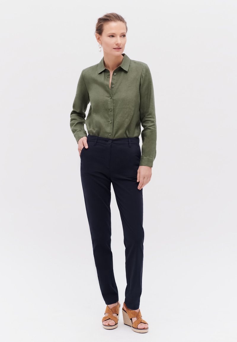 Olivgrön knapp-up skjorta, marinblå slim-fit byxor och tan platta sandaler; mjuk tyg och klassisk krage design.