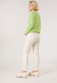 Light green knit sweater, cream fitted pants, and beige platform shoes. Textured sweater with ribbed design, pants with back pockets.