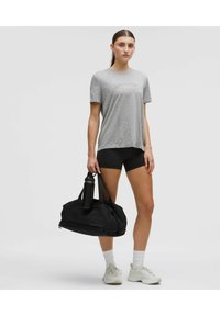 Grå kortärmad t-shirt, svarta shorts, svart gymväska och svart vattenflaska. Vita sneakers med vita strumpor. Enkelt, atletiskt design.