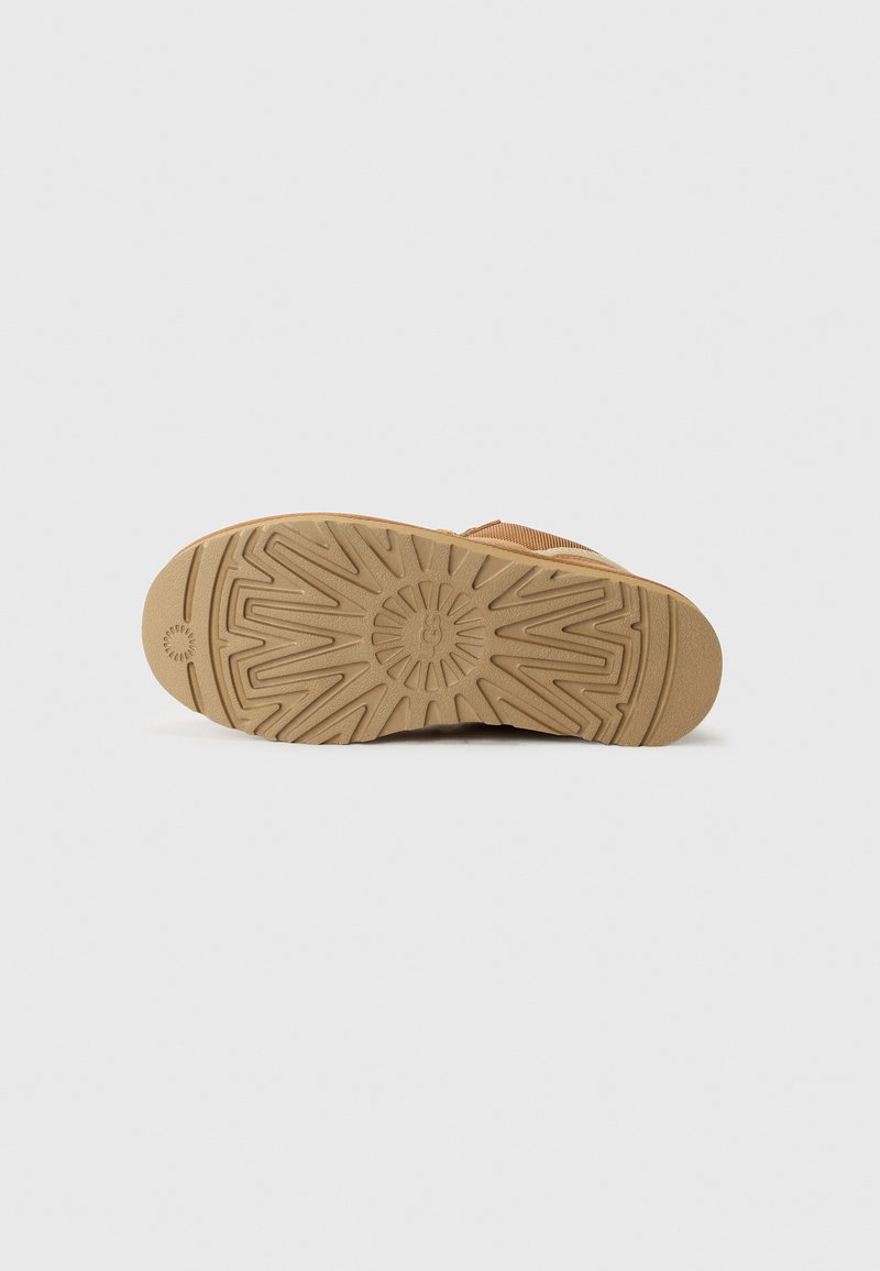 Braune Gummisohle mit strukturiertem Muster, die in der Mitte ein kreisförmiges Emblem und ein Sternenburst-Design für besseren Halt aufweist.