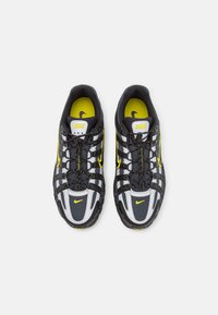 Nike sneakers with a black mesh upper, grey accents, and yellow details. Features a lace system and rubber sole for traction.