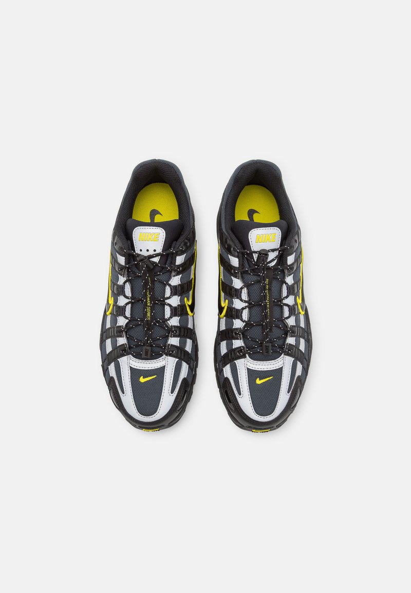 Zapatillas Nike con parte superior de malla negra, acentos grises y detalles amarillos. Presentan un sistema de cordones y una suela de goma para mayor tracción.