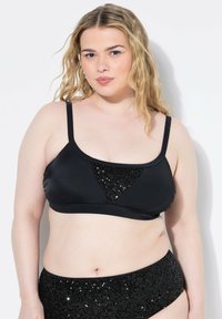 Top bikini nero con spalline sottili, caratterizzato da un'accenno triangolare di paillettes al centro. Materiale liscio con un design aderente.