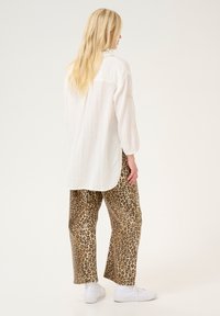 White, textured long-sleeve shirt paired with loose leopard-print pants. Bright white sneakers complete the outfit.