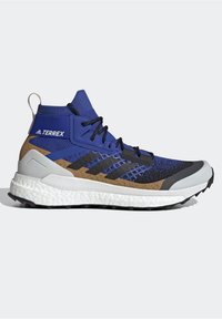 Chaussure de trail running montante Adidas Terrex bleue, marron et noire avec semelle blanche amortie et lacets noirs sur fond uni.