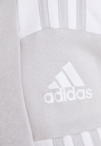 Lys grå Adidas hettegenser i et strukturert stoff. Har hvite tre striper og et logopatch, som fremhever sporty designelementer.