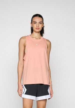 Peach tank top in soft fabric with a crew neckline and wide armholes, featuring a small white logo. Paired with black shorts with white accents.