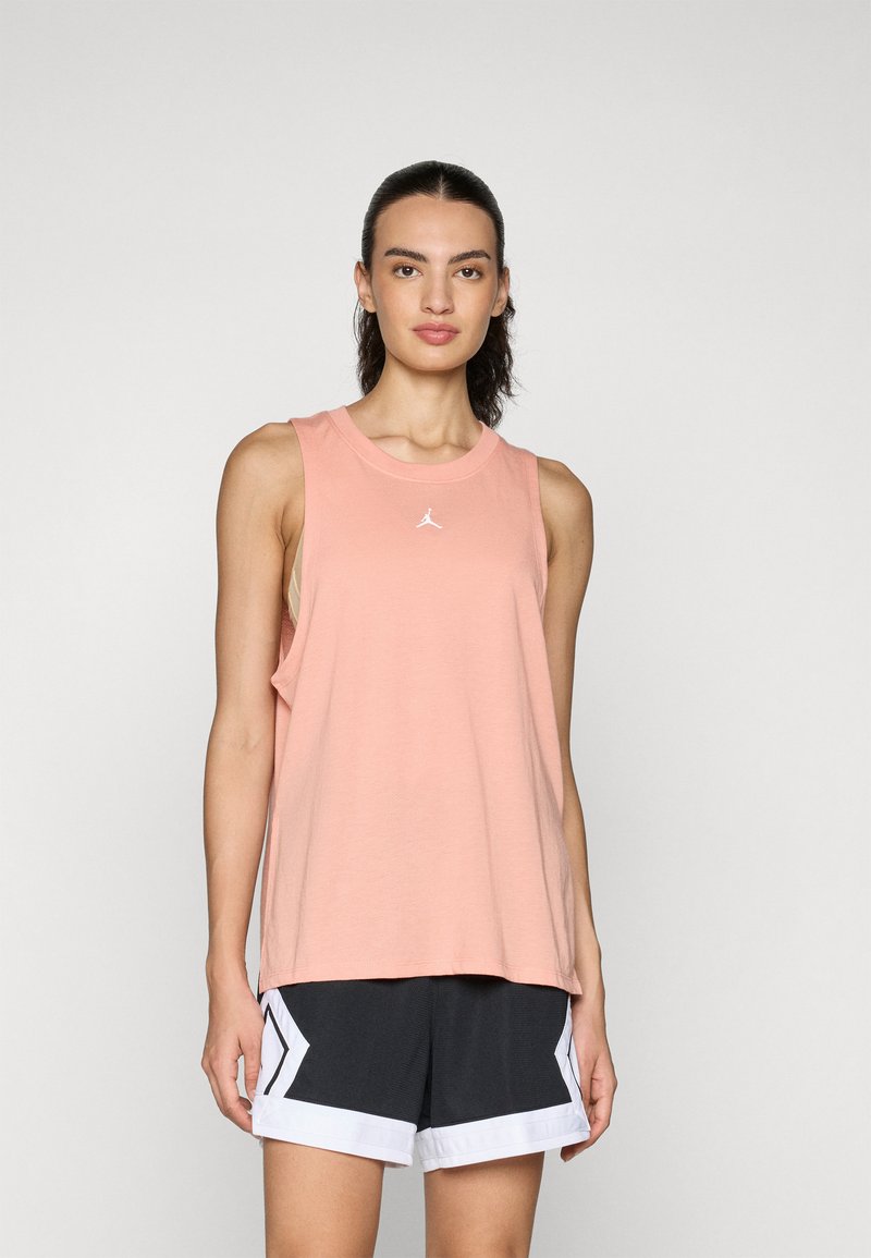 Peach tank top in soft fabric with a crew neckline and wide armholes, featuring a small white logo. Paired with black shorts with white accents.