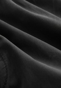 Tissu noir avec texture de tissage visible et coutures, présenté en plis doux et en gros plan.