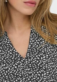 Schwarz-weiße Bluse mit V-Ausschnitt und Blättermuster, aus leichtem Stoff mit glatter Textur.