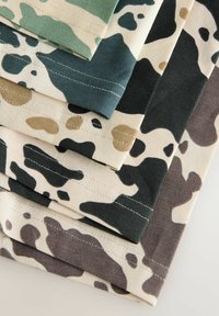 Empilement de morceaux de tissu avec divers motifs camouflage en vert, beige, noir, marron et sable, montrant les bords cousus.