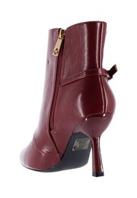 Stivaletto alla caviglia color bordeaux con tomaia in pelle sintetica, tacco a stiletto sottile, cerniera laterale e cinturino decorativo con dettagli dorati.
